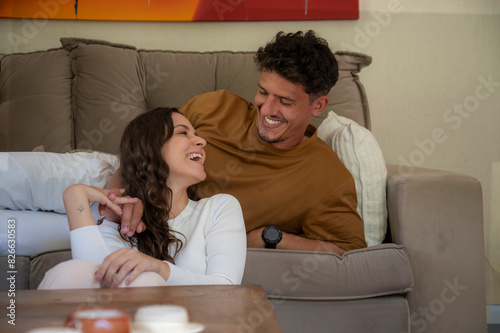 Jovem Casal sorrindo na sala de tv sentado no sofa com mesa centro no primeiro plano, família feliz celebrando. photo