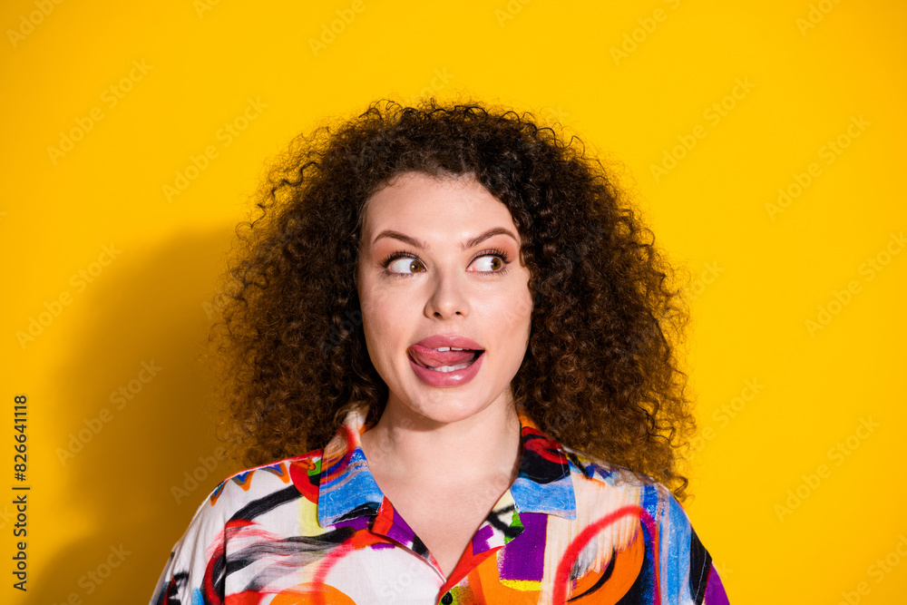 Photo portrait of lovely young lady lick teeth look empty space dressed stylish colorful print garment isolated on yellow color background Photo portrait of lovely young lady lick teeth look empty space dressed stylish colorful print garment isolated on yellow color background