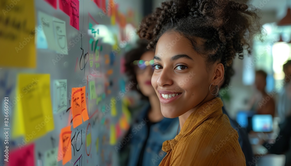 Young professional woman smiling at the camera in a modern office setting with colorful sticky notes brainstorming and teamwork. Young professional woman smiling at the camera in a modern office setting with colorful sticky notes brainstorming and teamwork.