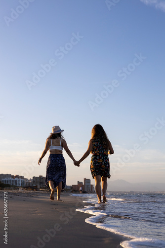 Couple of girls on their backside holding hands walking on the beach