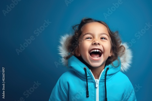 A young girl is smiling and wearing a blue coat with a hood. She is wearing a fur-lined hood and she is happy photo