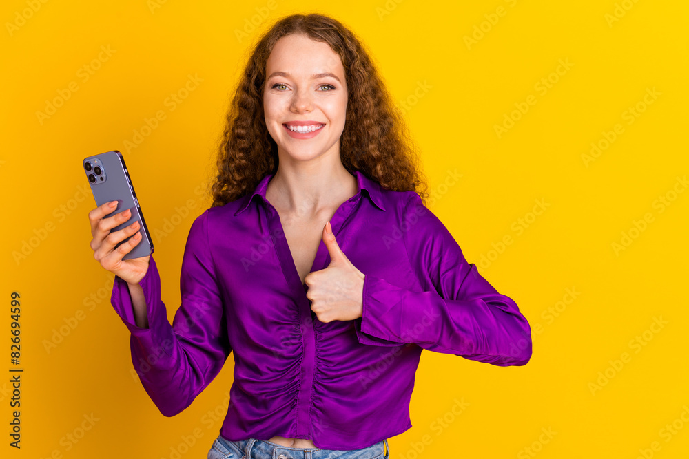 Photo portrait of lovely young lady hold device show thumb up dressed stylish violet garment isolated on yellow color background