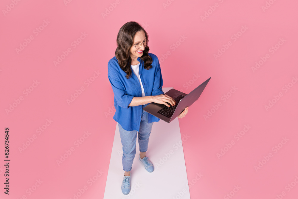 Full body photo of attractive retired woman podium hold netbook top view dressed blue clothes isolated on pink color background