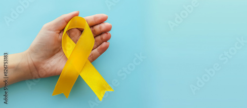 hand holding a yellow ribbon for cancer awareness on a light blue background with copy space for text