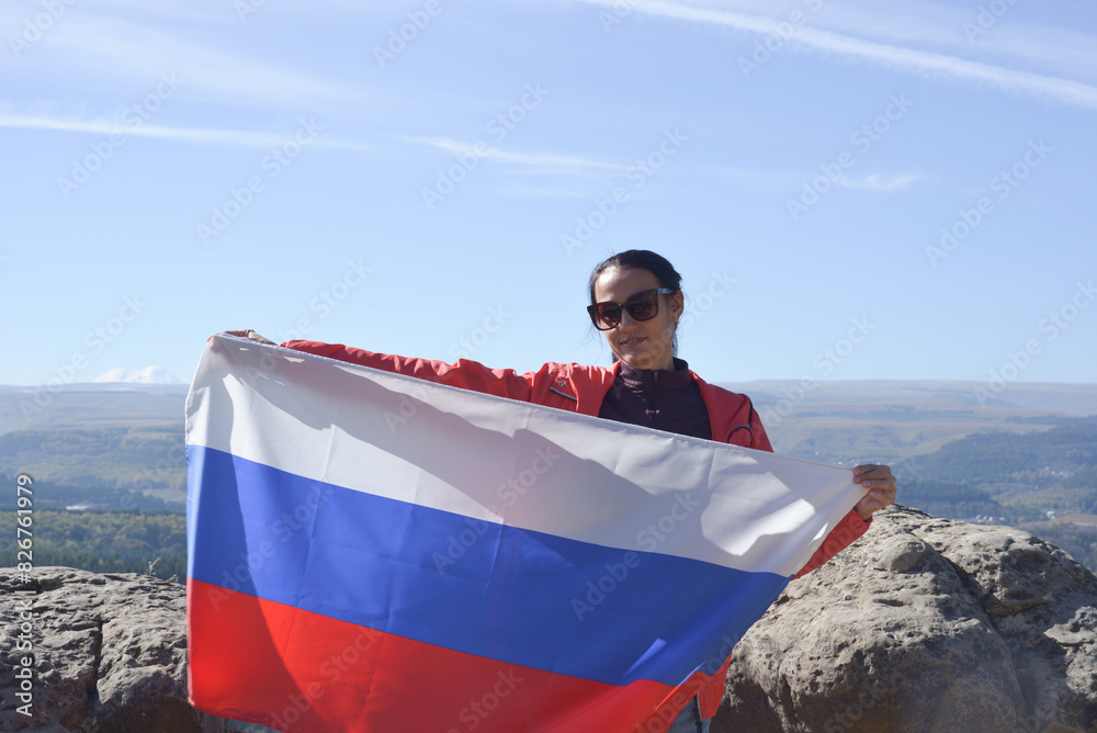 The Russian flag is on the shoulders of a girl standing against the backdrop of the Caucasus mountains. Unity Day in Russia.