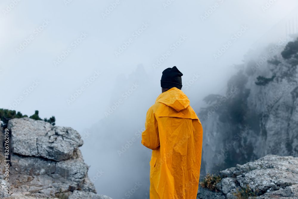 A solitary figure in a vibrant yellow raincoat conquers the majestic mountain peak, shrouded in mysterious fog A solitary figure in a vibrant yellow raincoat conquers the majestic mountain peak, shrouded in mysterious fog