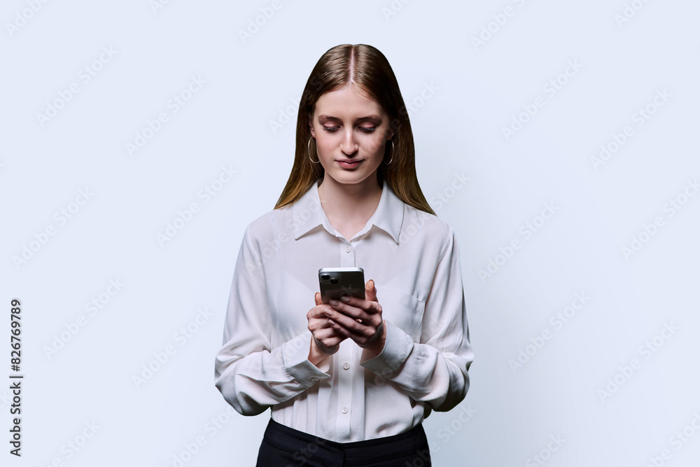 Teenage student girl in shirt holding smartphone in hands on white studio background Teenage student girl in shirt holding smartphone in hands on white studio background