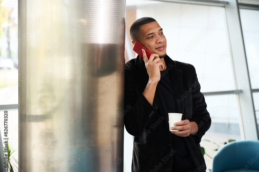 Amused manger talking on phone while leaning against metal pillar Amused manger talking on phone while leaning against metal pillar
