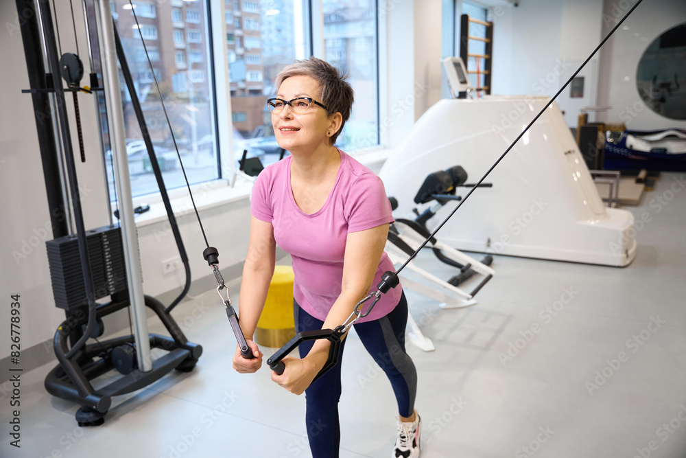 Fototapeta premium Middle aged caucasian woman doing sport exercise for chest muscles in gym