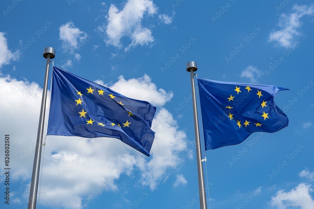 Two EU flags waving against a blue sky with clouds.