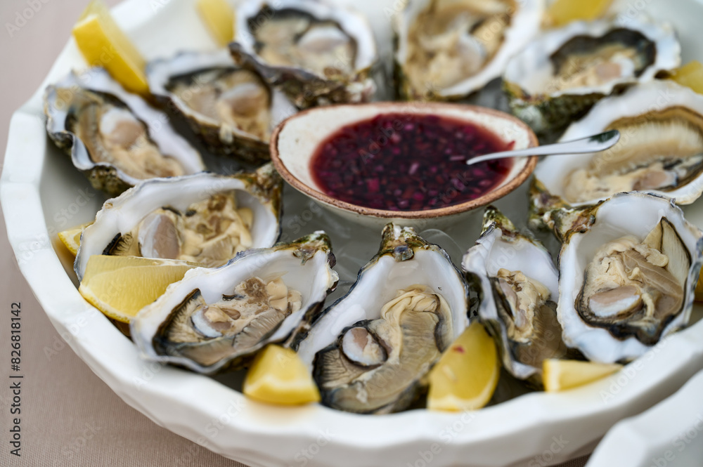 fresh shucked oysters on a plate with lemon slices and red sauce in a bowl. Close up shot 