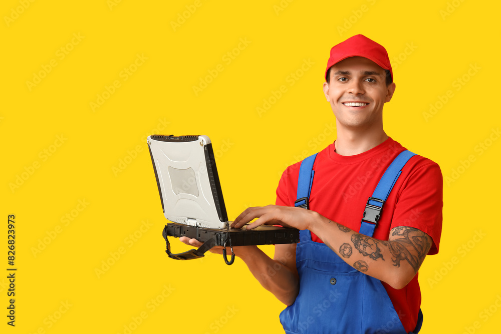 Male car mechanic with laptop on yellow background Male car mechanic with laptop on yellow background