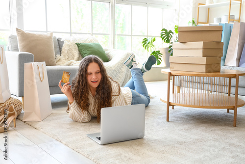 Young woman with credit card, laptop, bags and boxes shopping online at home photo