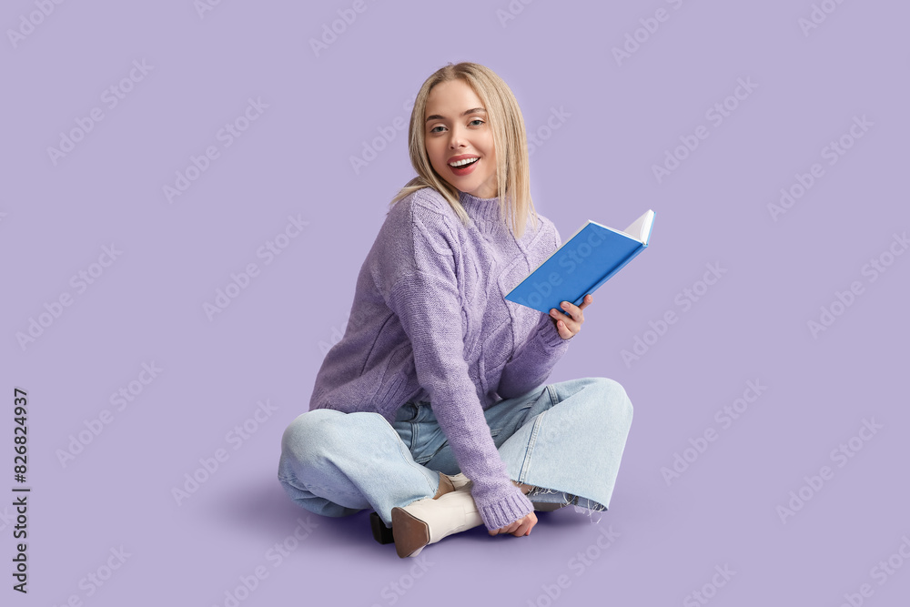 Beautiful young happy woman with book sitting on lilac background