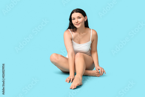 Body positive woman in underwear sitting on blue background