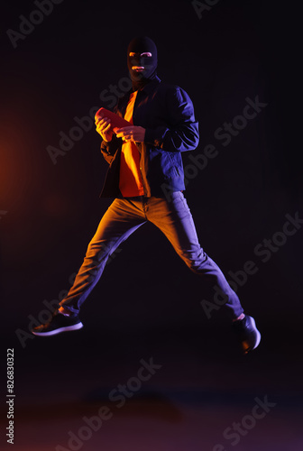 Handsome young man in balaclava with wireless portable speaker jumping on black background