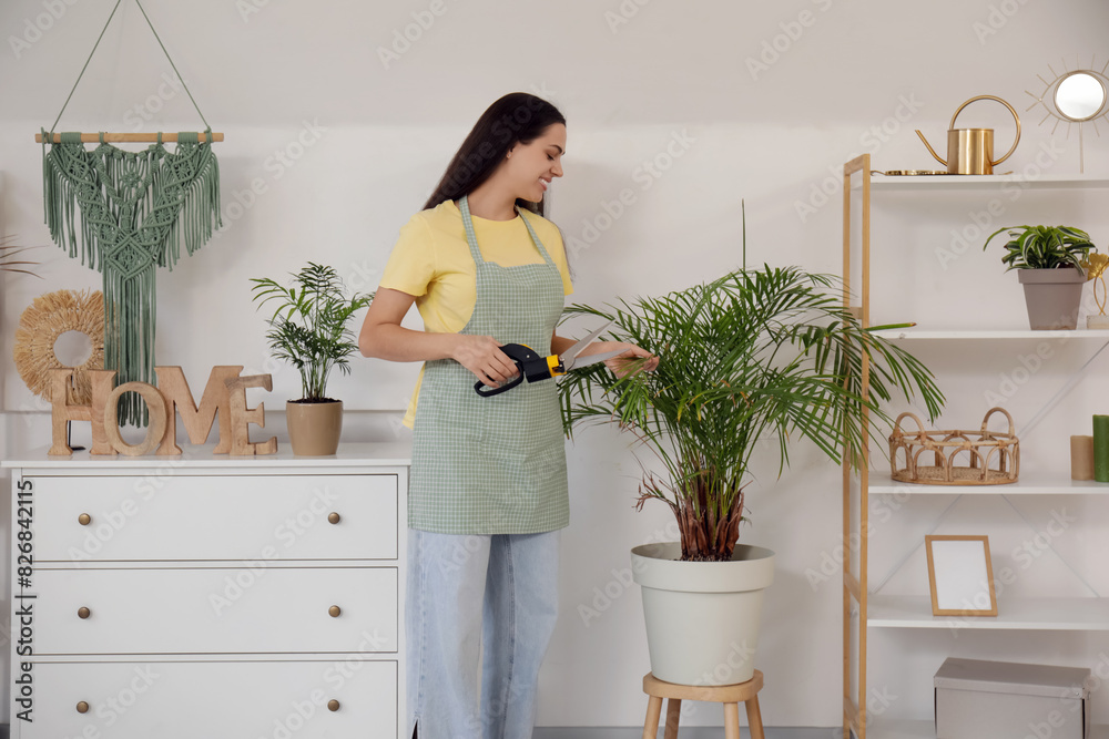Young happy woman cutting houseplants with pruner at home