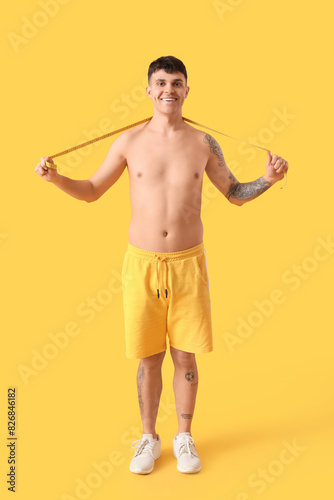 Young man with measuring tape on yellow background. Weight loss concept