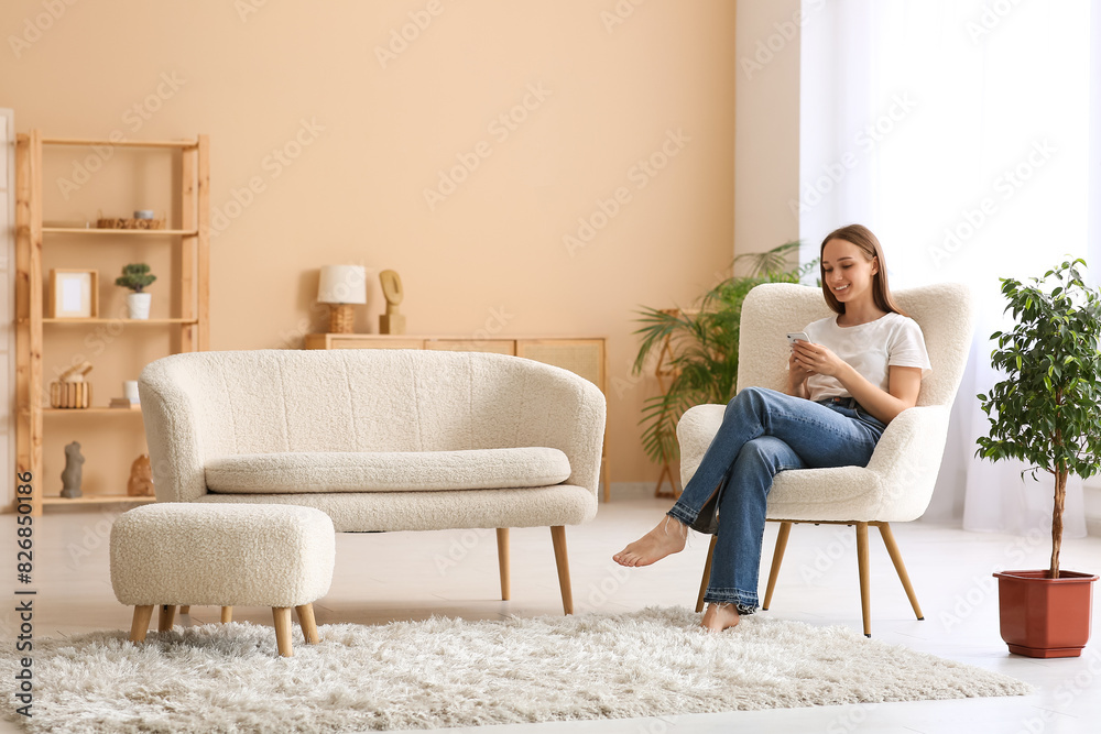 Young pretty woman using mobile phone and sitting on armchair in living room Young pretty woman using mobile phone and sitting on armchair in living room
