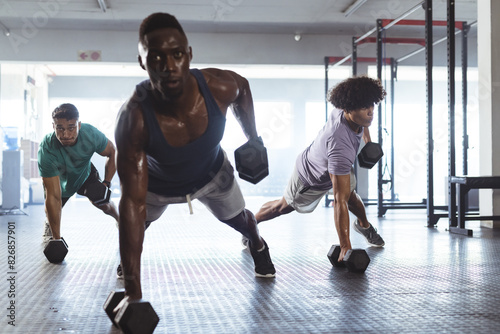 At gym, three young, fit, and diverse men training with dumbbells photo
