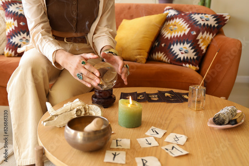 Young witch with crystal ball on table at home, closeup photo