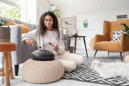 Vászonkép Young African-American witch playing glucophone on floor at home