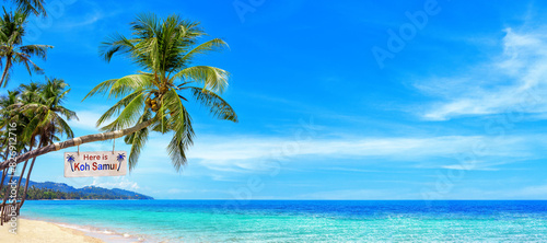 Fototapeta Naklejka Na Ścianę i Meble -  Here is Koh Samui - wooden sign on palm tree, paradise tropical island, sea sand beach panorama landscape, ocean, sun sky cloud, Surat Thani, Thailand, summer holidays, vacation, Southeast Asia travel