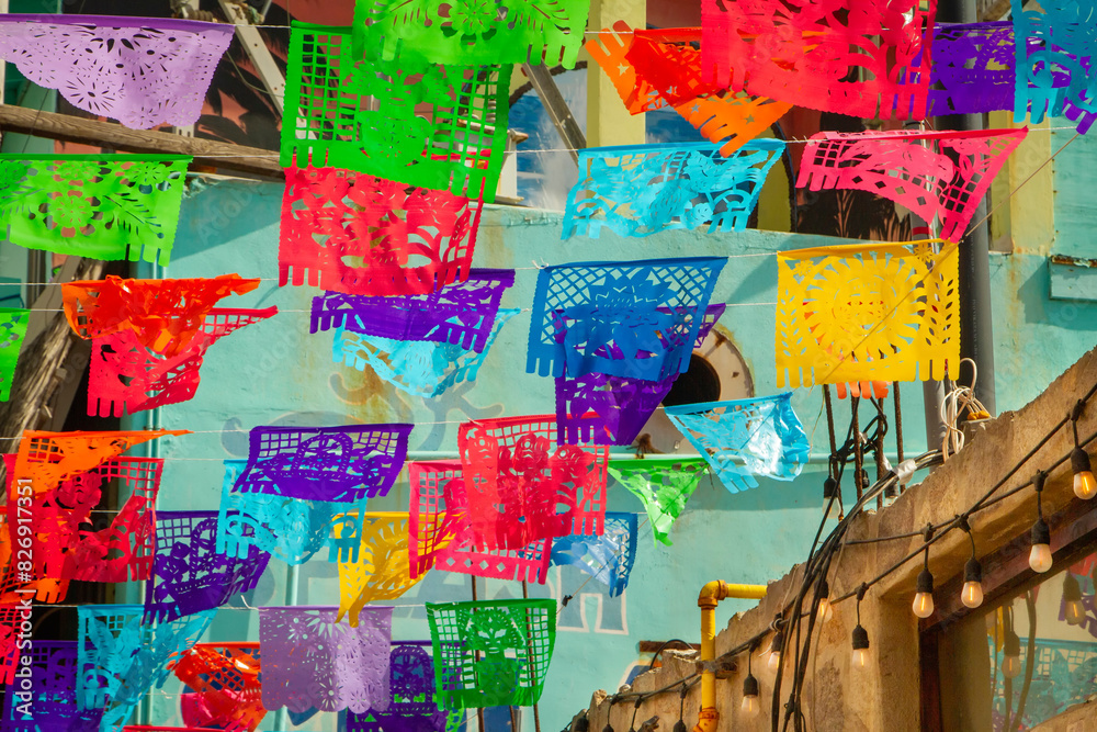 Fototapeta premium Colorful festive flags hanging against a colorful building background in Rosarito Mexico