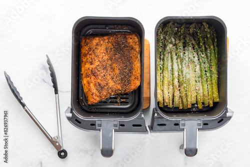 Air fryer compartments of cooked salmon and asparagus spears with seasoning. photo