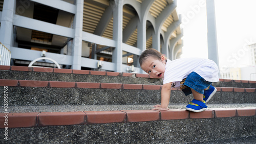 Portrait of an Asian little boy joyfully climbing up a wide staircase. A mischievous toddler kid. Muscle development and learning. Children aged one year and six months.