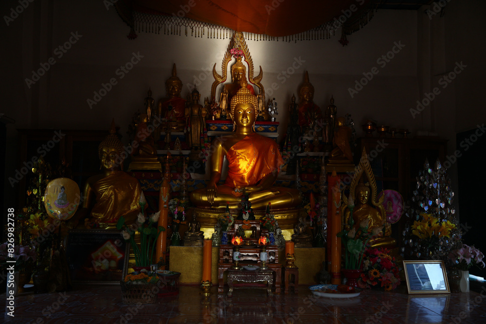 There are several Buddha statues on the shelf, one large and with a silver bush on the right and a gold one on the left There are several Buddha statues on the shelf, one large and with a silver bush on the right and a gold one on the left