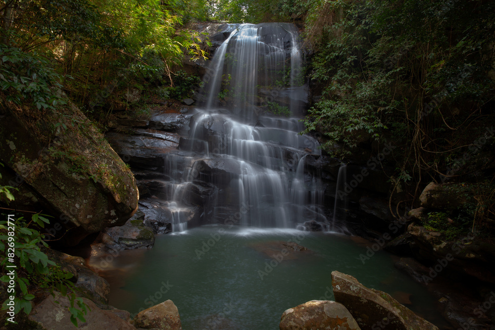 Obraz premium A medium-sized waterfall among rocks and bushes, with a water source and submerged rocks