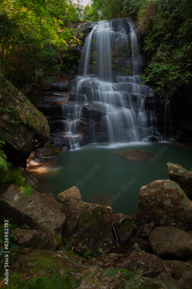 Obraz premium A medium-sized waterfall among rocks and bushes, with a water source and submerged rocks