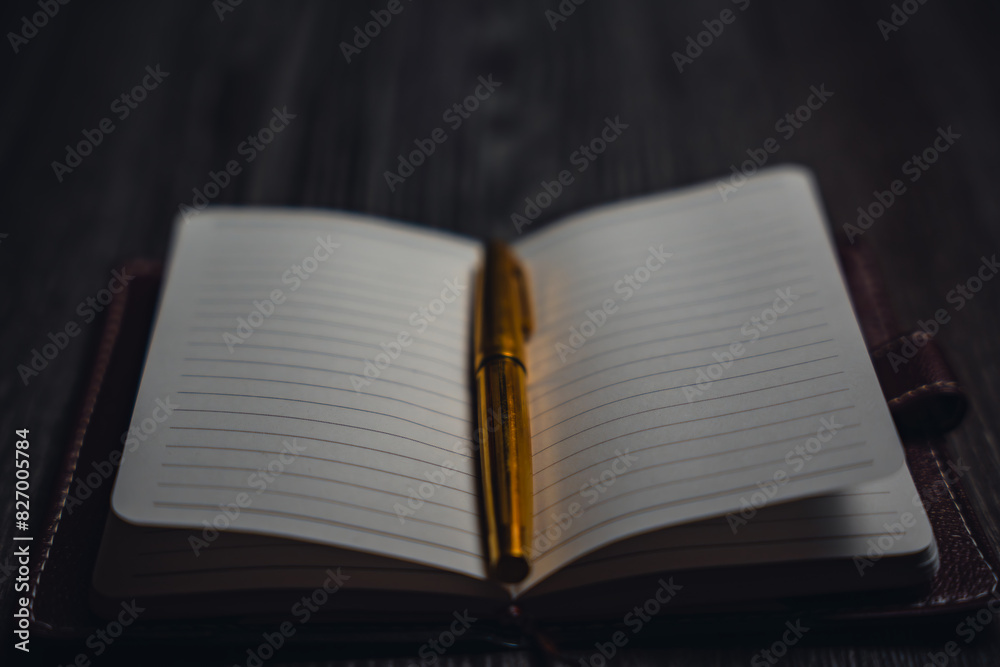Naklejka premium A notebook with a gold pen on the table in the candlelight