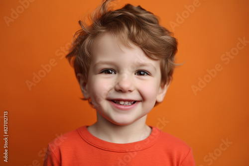 A cute preschooler with dimpled cheeks and a wide grin, standing against a cheerful coral backdrop.