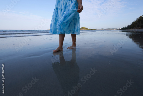 A little girl walks barefoot along the beach in the morning, leaving footprints on the sand and reflections in the water. close-up of a young girl's legs on the beach. calmness and tranquility. touris photo