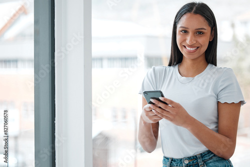 Portrait, woman and smartphone by window in office for social media, communication and connect for company. Creative businessperson, happy and text in workplace for networking, technology or contact