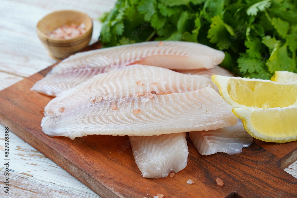 Fresh tilapia fish fillet sliced for steak or salad with herbs spices and lemon Fresh tilapia fish fillet sliced for steak or salad with herbs spices and lemon