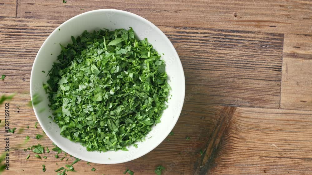 A chef sprinkles chopped fresh green parsley in a white bowl on wooden kitchen table to prepare a healthy meal, top view. Food close up A chef sprinkles chopped fresh green parsley in a white bowl on wooden kitchen table to prepare a healthy meal, top view. Food close up