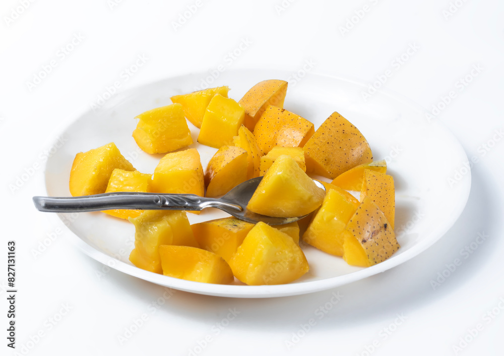 Ripe delicious sliced mangoes on white background served ready to eat with spoon on white plate.