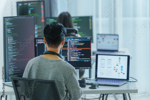 Asian software developers working on multiple screens displaying code and application diagrams in a modern office