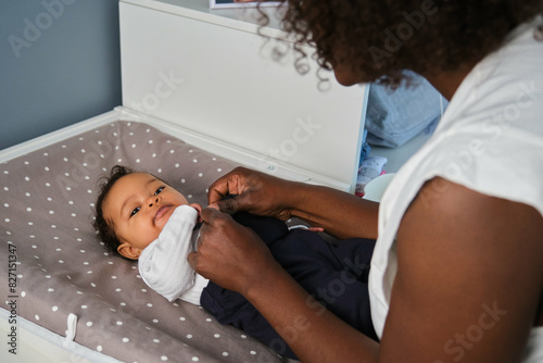 African mother is dressing up her baby girl on a changing table. photo