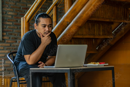 Young Asian man, digital nomad working remotely from cafe, using laptop and smartphone. young Asian men are hanging out in a cafe with an industrial theme