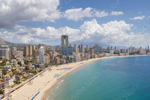 Aerial drone photo of the beautiful town of Benidorm in Spain showing the south beach Promenade golden sandy beach and apartments on a sunny summers day with a blue sky and a few clouds