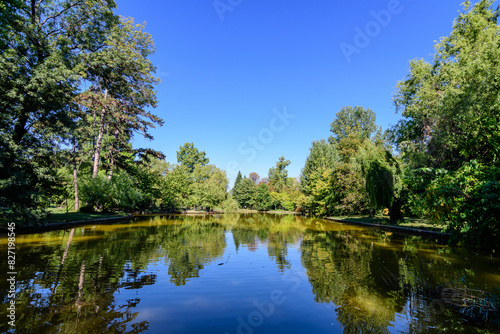 Vivid green landscape with old large linden trees and small boats near the lake in Cismigiu Garden (Gradina Cismigiu), a public park in the city center of Bucharest, Romania, in a sunny spring day