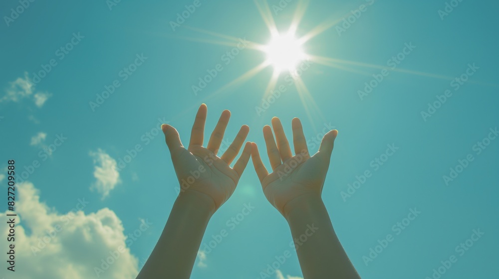 Two hands reach towards the radiant sun in a clear blue sky, creating a starburst effect as sunlight diffuses through the fingers. 