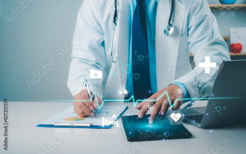 Male doctor using tablet to review treatment plan and write document reports in hospital office, Healthcare worker and doctor service, Digital laptop in modern office, Medical technology concept. photo
