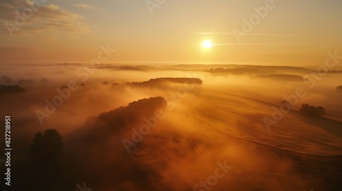 Aerial view of a sunrise casting golden light over foggy fields and trees