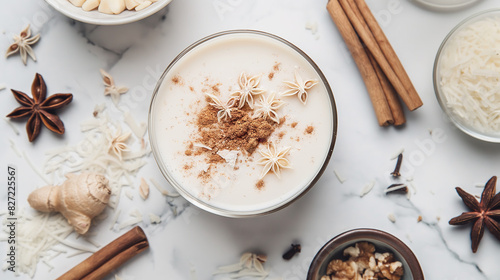 creamy rice horchata milk in a glass with cinnamon and star anise, surrounded by small bowls of ginger powder and cardamom on a white marble surface