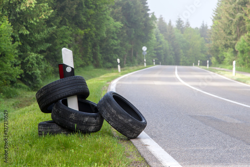 Along a country road, several illegally dumped old tires are stuck on a roadside marker. This bizarre scene highlights a lack of understanding for environmental protection.